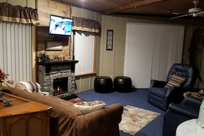 Un salon avec une cheminée en pierre, un téléviseur fixé au-dessus, un fauteuil en cuir et un tapis bleu.