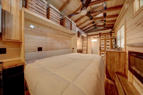 A wooden interior with a large bed, wooden walls, and a ceiling fan.