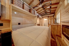 Un interior de madera con una cama grande, paredes de madera y un ventilador de techo.