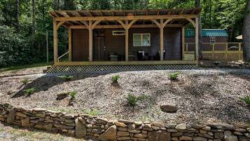 Una cabaña con porche cubierto, pared de piedra y una pequeña terraza.