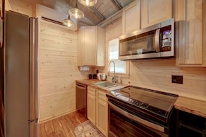 Cocina compacta con paredes de madera, un refrigerador de acero inoxidable, un microondas y una estufa.