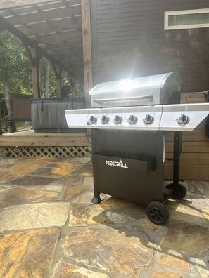 A portable grill with four burners and a side shelf, placed on a stone patio.