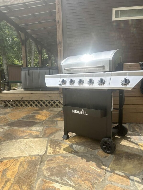Una parrilla portátil con cuatro quemadores y una repisa lateral, ubicada en un patio de piedra.