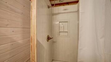 Une salle de bain aux murs lambrés, avec une douche, une porte blanche et une serviette accrochée sur le côté droit.