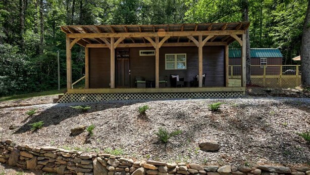 A cabin with a covered porch, stone wall, and a small deck area.