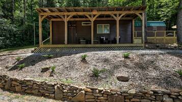 A cabin with a covered porch, stone wall, and a small deck area.