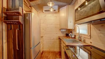Cocina compacta con paredes de madera, un refrigerador de acero inoxidable, un lavamanos y un horno empotrado.