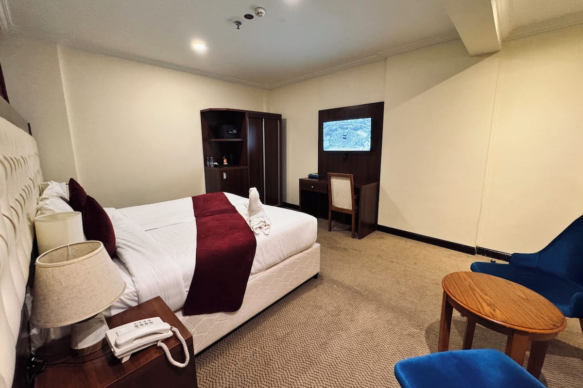 A hotel room with a bed, a desk, a TV, a chair, and a lamp.
