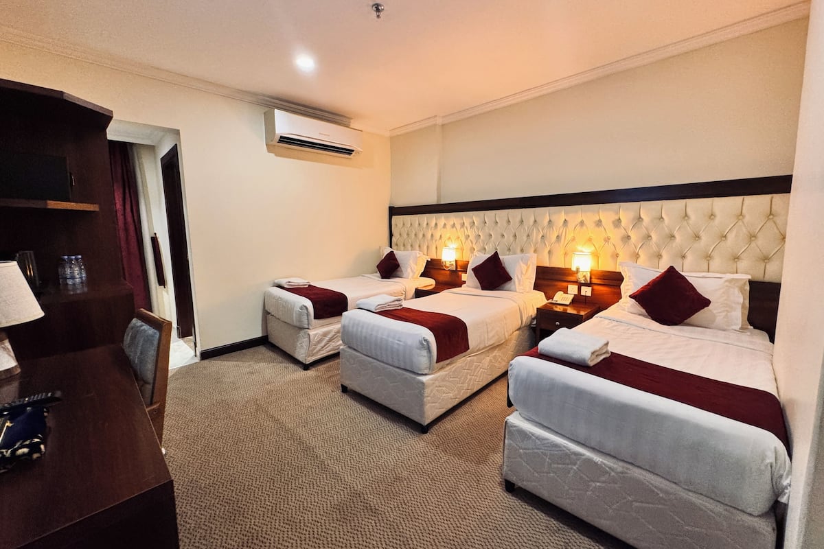 A hotel room with two beds, a desk, and a chair. There is an air conditioning unit on the wall.