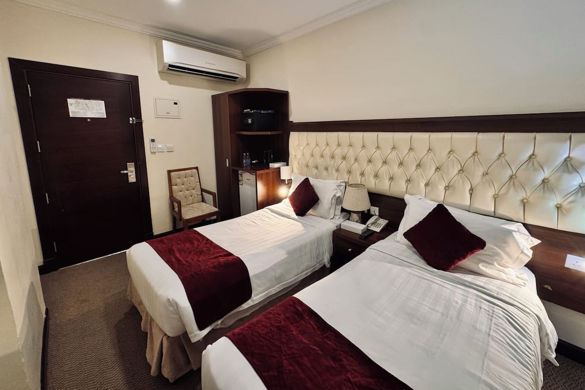 A hotel room with two beds, a chair, a desk, a phone, and an air conditioning unit.