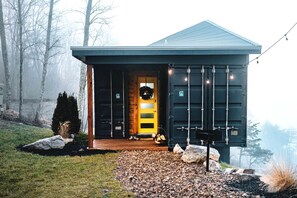 A modern building with a dark exterior, a yellow door, and a small porch area with a bench and a wreath. - Romantic Container Beautifully Design with Deck in Georgia (Rising Fawn)