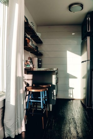 A narrow kitchen with wooden walls, a built-in oven, and a window with a curtain.