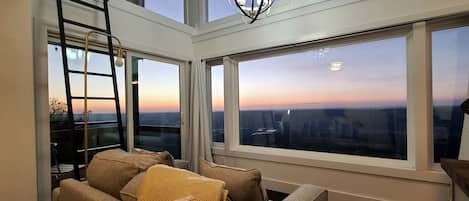 A high-rise room with large windows, a ladder, and a chandelier.