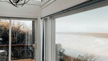 Una habitación con ventanas amplias, una terraza de madera y una lámpara moderna.