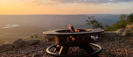 A portable fire pit on a rocky surface with a view of a distant landscape.