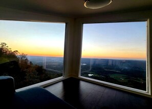 Une pièce dotée de grandes fenêtres donnant sur un panorama urbain au coucher du soleil.