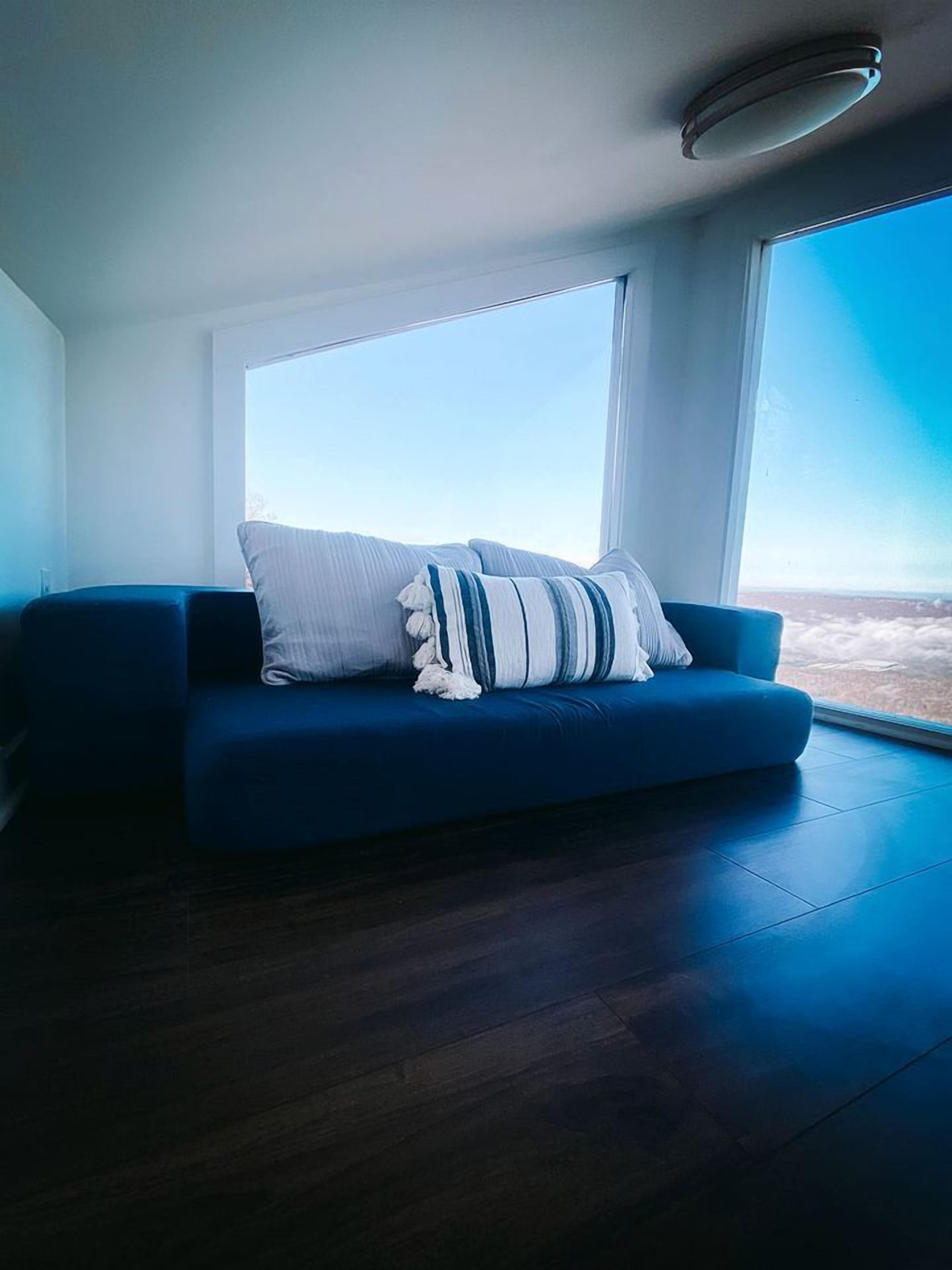 Un salon moderne avec un canapé bleu, une grande fenêtre et un luminaire au plafond.