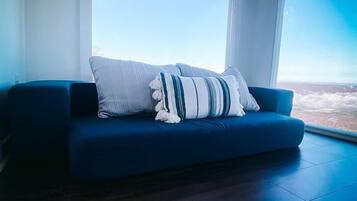 Un salon moderne avec un canapé bleu, une grande fenêtre et un luminaire au plafond.