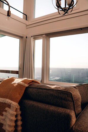A high-rise room with large windows, a sofa, a throw blanket, and a hanging light fixture. - Romantic Container Beautifully Design with Deck in Georgia (Rising Fawn)