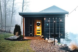 A modern building with a dark exterior, a yellow door, and a small porch area with a bench and a wreath. - Romantic Container Beautifully Design with Deck in Georgia (Rising Fawn)