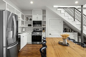 Une cuisine moderne avec des meubles blancs, des appareils en acier inoxydable, une table à manger en bois et un escalier.