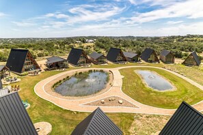 A modern resort with unique triangular buildings, a central pond, and a well-maintained lawn. - Three Stylish A-Frames Perfect for a Group Escape in Texas (New Braunfels)