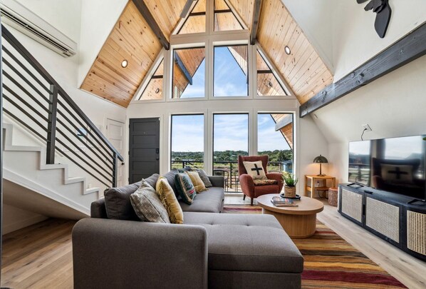Un loft spacieux avec un haut plafond, un grand canapé, une télévision et un escalier.