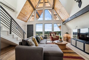 A spacious loft with a high ceiling, a large sofa, a television, and a staircase.