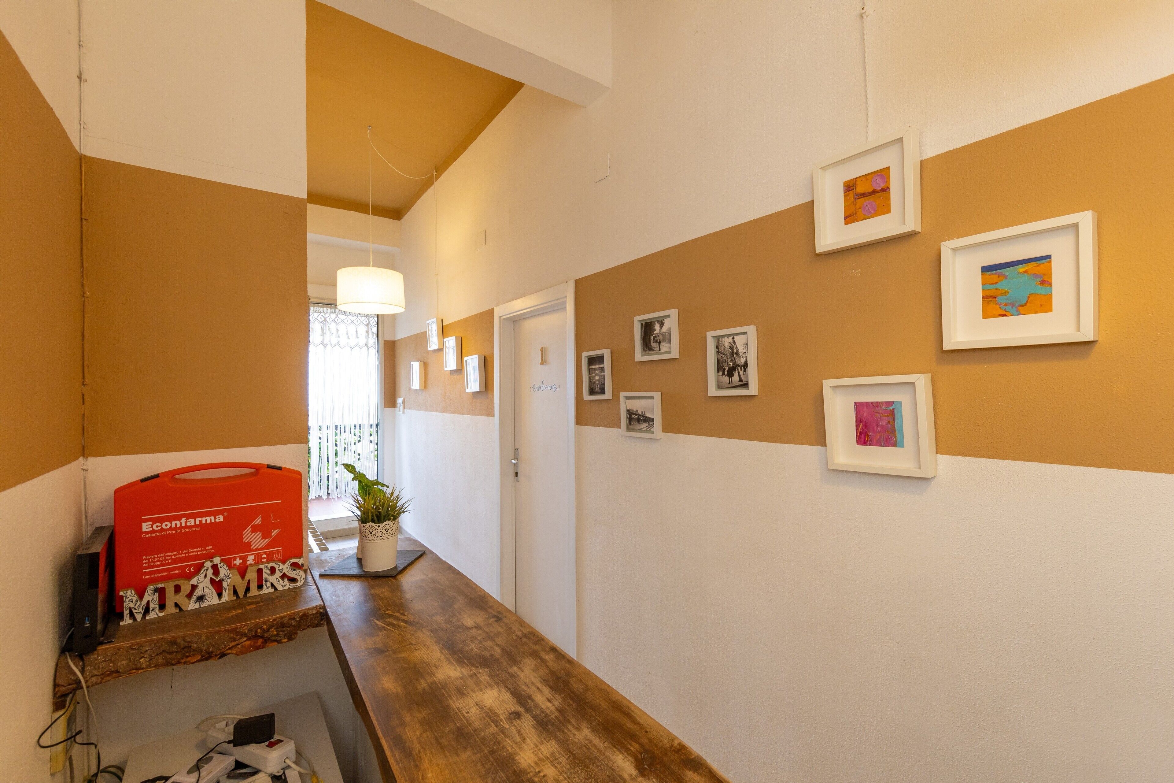 Un couloir avec un banc en bois, des tableaux encadrés accrochés au mur et une boîte Econfarma rouge.