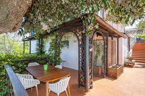 Un patio al aire libre con una mesa y sillas de madera, una pérgola con plantas trepadoras y una escalera de ladrillo.