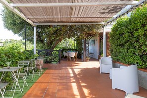Un patio al aire libre con pérgola, mesas, sillas y vistas al entorno verde.