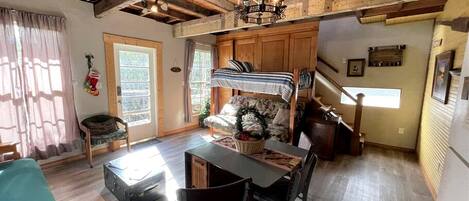 Interior acogedor de una cabaña con zona de comedor, vigas de madera, una araña y una escalera que sube a un nivel superior.