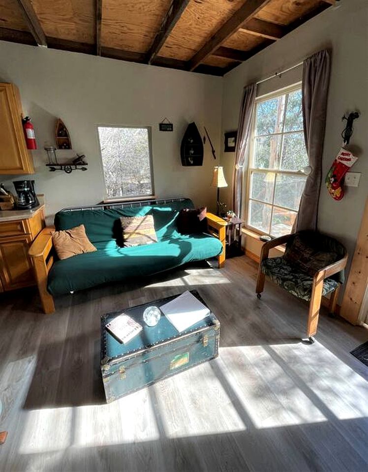 A cozy room with a green sofa, a wooden chair, a suitcase, and a window with curtains.