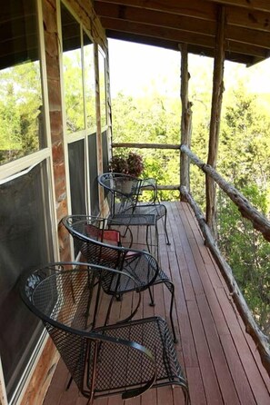 Una terraza de madera con sillas y una mesa de metal, con vistas a un área boscosa.