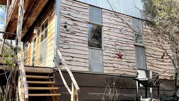 A two-story building with a wooden staircase leading to a deck, surrounded by dry vegetation.