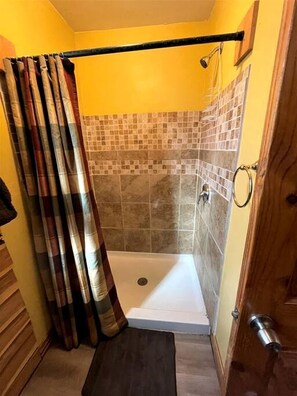 A shower with a tiled wall, a curtain, and a wooden door.
