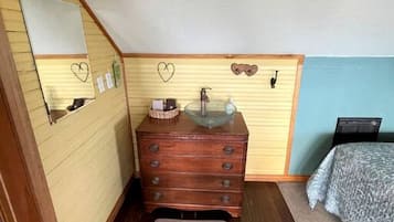 A small, cozy room with a wooden dresser, a mirror, a sink, a bed, and a small rug.