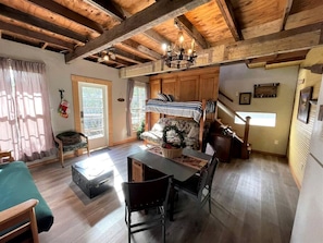 A cozy cabin interior with a dining area, wooden beams, a chandelier, and a staircase leading to an upper level. - Two-Story Cabin Rental for Large Groups along Hamilton Creek in Marble Falls, Texas (Marble Falls)