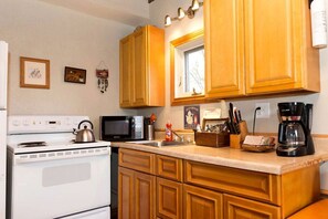 Una cocina con armarios de madera, estufa, microondas, cafetera y diversos utensilios de cocina.