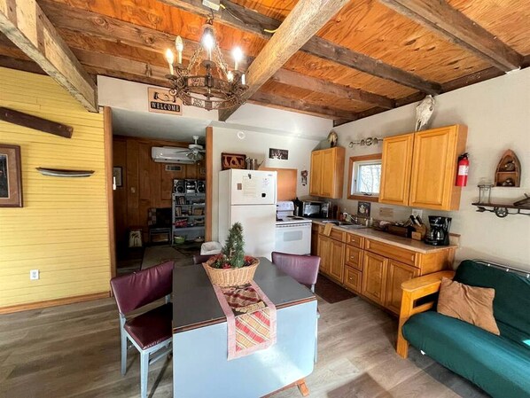 A cozy interior with a wooden ceiling, a kitchen area with wooden cabinets, a dining table with chairs, and a green sofa.
