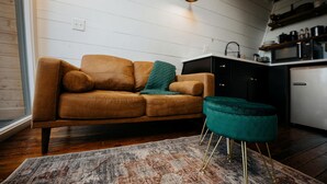 Un salon moderne avec un canapé, un pouf et un coin cuisine à l’arrière-plan.