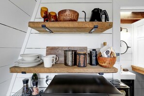 A kitchen with wooden shelves holding dishes, mugs, and a kettle.