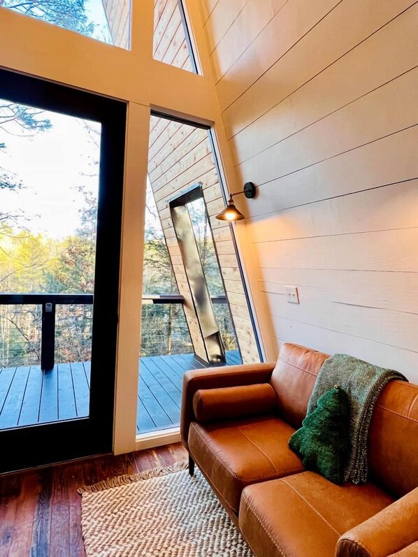 A room with a brown leather sofa, a woven rug, and a large window with a view of trees.