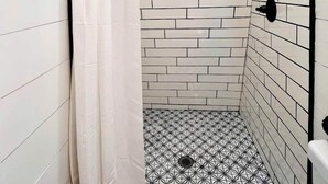 Une douche aux murs recouverts de carreaux blancs et au sol à motifs, avec un plafond en bois et une pomme de douche en métal.