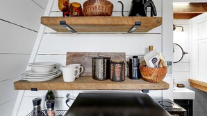 Une cuisine avec des étagères en bois où sont rangées de la vaisselle, des tasses et une bouilloire.