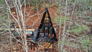 Una baita dal tetto a forma di triangolo, circondata da alberi e terreno sterrato.