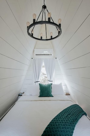 A narrow, high-ceilinged room with a bed, a chandelier, and a window with curtains. - Intimate Private A-Frame with Spa and Beautiful Outdoor Living in Georgia (Blue Ridge)