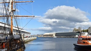A harbor with a large sailing ship docked on the left and a modern building in the background. - The View | Panoramic River Views | Sleeps 12 (Sandy Bay)