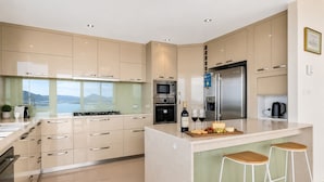 A modern kitchen with a central island, stainless steel appliances, and a view of the outdoors. - The View | Panoramic River Views | Sleeps 12 (Sandy Bay)