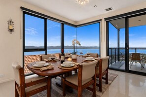 A dining area with a table set for four, large windows, and a view of the sea. - The View | Panoramic River Views | Sleeps 12 (Sandy Bay)